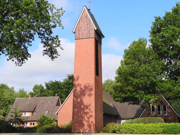 Friedenskirche Augustfehn Die Friedenskirche Augustfehn ist ein eindrucksvoller roter Backsteinturm, umgeben von grünen Büschen und Bäumen.