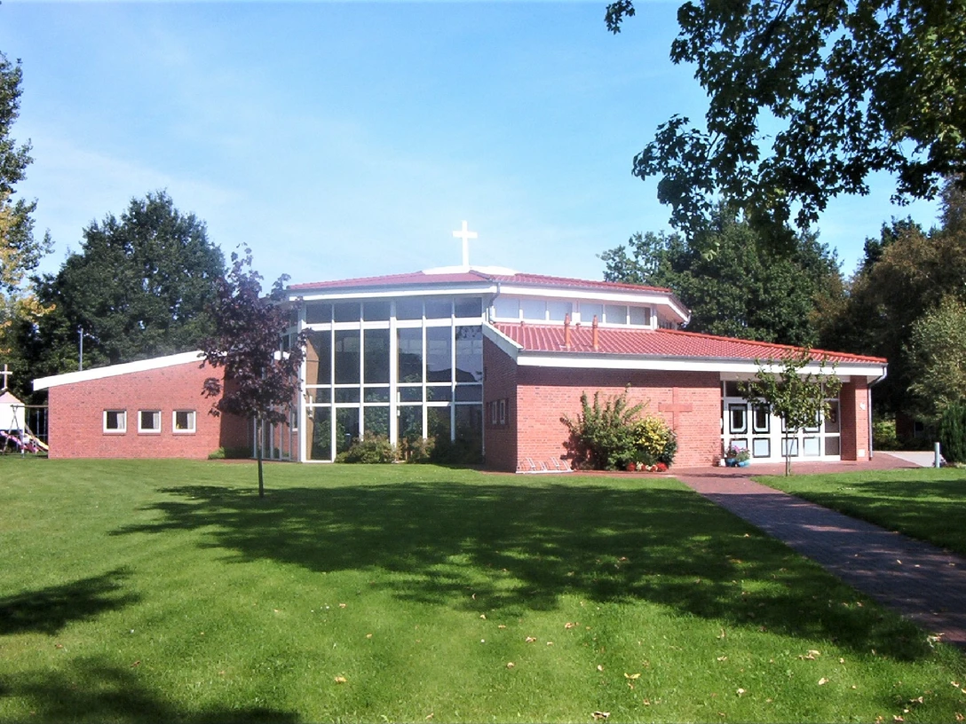 Moderne Freikirche mit rotem Ziegeldach und großem Glasfenster, eingebettet in eine grüne Landschaft.