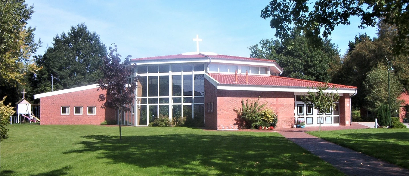 Moderne Freikirche mit rotem Ziegeldach und großem Glasfenster, eingebettet in eine grüne Landschaft.