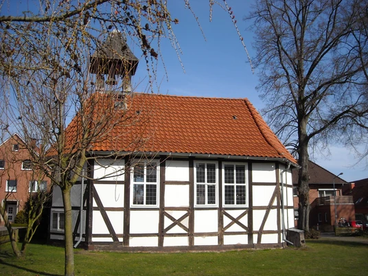 Mardorfer Kapelle Fachwerkgebäude mit rot gedecktem Dach und Glockenturm, umgeben von Bäumen und Wiese vor blauem Himmel.