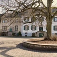 Lindenhof Ein historisches Steingebäude mit grünen Fensterläden und einem weitläufigen, gepflasterten Hof mit einem großen, kahlen Baum im Vordergrund.A historic stone building with green shutters and a spacious, cobbled courtyard with a large, bare tree in the foreground.