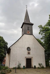 Bordenau Kirche Eine historische Kirche mit spitzem Turm unter bewölktem Himmel, umgeben von Bäumen und Pflanzen.