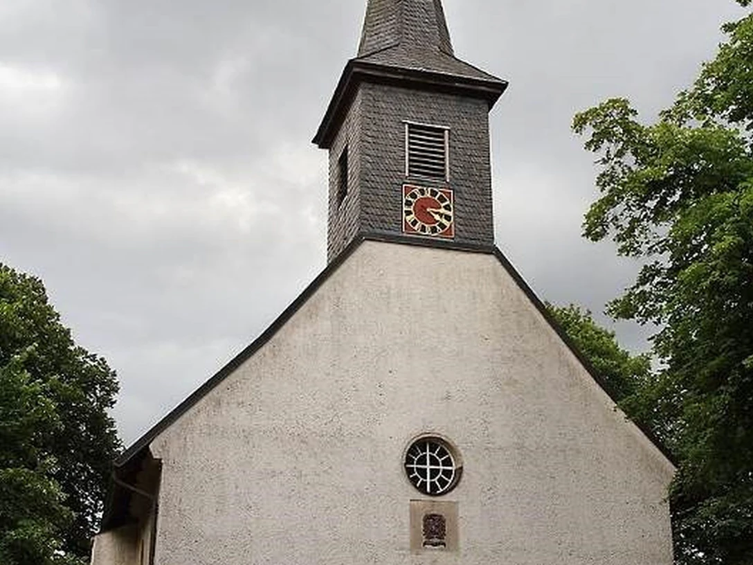 Bordenau Kirche Eine historische Kirche mit spitzem Turm unter bewölktem Himmel, umgeben von Bäumen und Pflanzen.