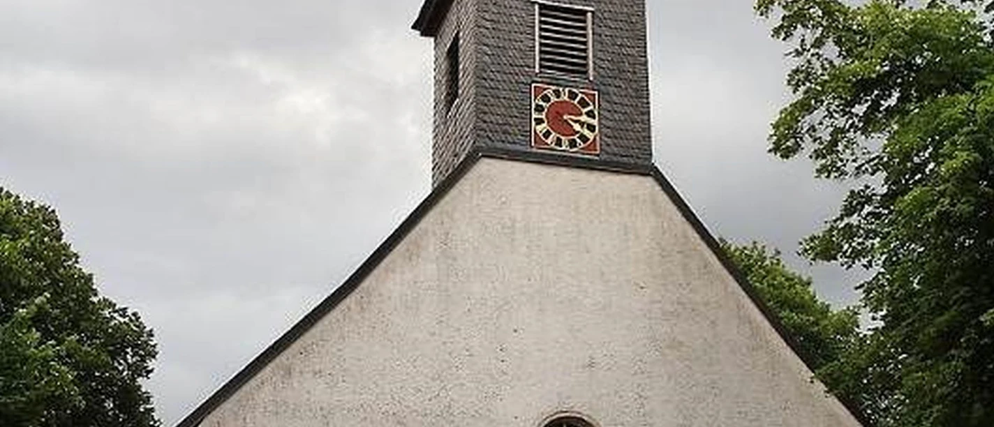 Bordenau Kirche Eine historische Kirche mit spitzem Turm unter bewölktem Himmel, umgeben von Bäumen und Pflanzen.
