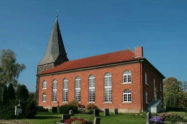 Niedernstöcken Kirche Die Backsteinkirche von Niedernstöcken mit ihrem spitzen Kirchturm steht umgeben von grünen Bäumen.