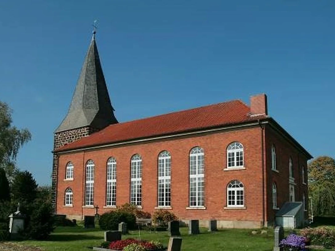 Niedernstöcken Kirche Die Backsteinkirche von Niedernstöcken mit ihrem spitzen Kirchturm steht umgeben von grünen Bäumen.