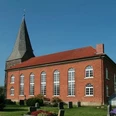 Niedernstöcken Kirche Die Backsteinkirche von Niedernstöcken mit ihrem spitzen Kirchturm steht umgeben von grünen Bäumen.