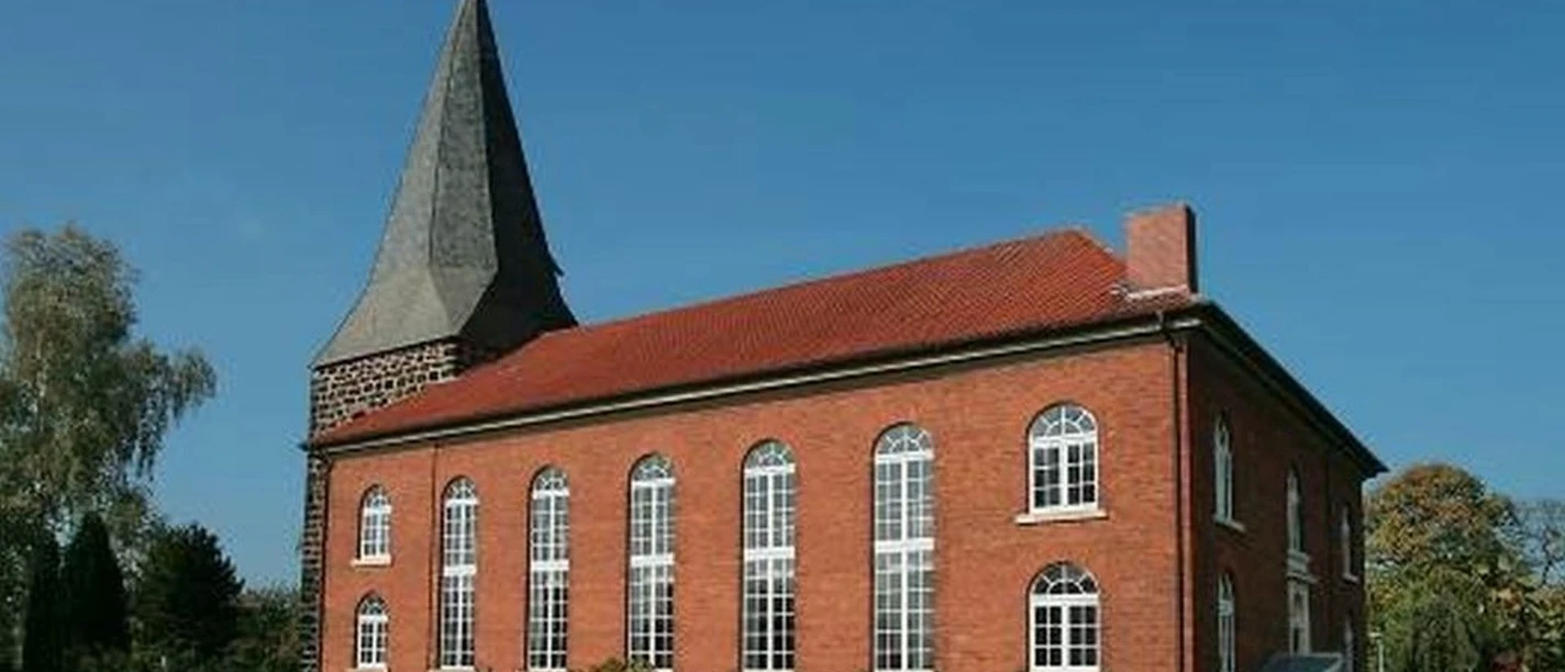 Niedernstöcken Kirche Die Backsteinkirche von Niedernstöcken mit ihrem spitzen Kirchturm steht umgeben von grünen Bäumen.