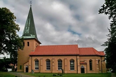 Kirche in Schwarmstedt Backsteinkirche in Schwarmstedt mit grünem Turm und rotem Dach. Umgeben von Bäumen und Wolken.
