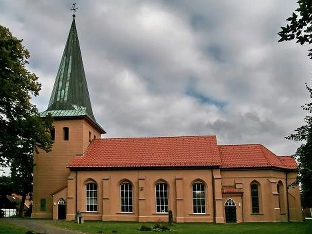 Kirche in Schwarmstedt Backsteinkirche in Schwarmstedt mit grünem Turm und rotem Dach. Umgeben von Bäumen und Wolken.
