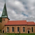 Kirche in Schwarmstedt Backsteinkirche in Schwarmstedt mit grünem Turm und rotem Dach. Umgeben von Bäumen und Wolken.