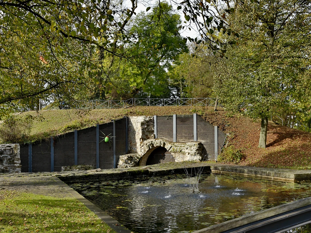 Neustadt Erichsberg Ein runder, von Bäumen gesäumter Teich vor einem alten Steinbogen in ruhiger naturnaher Umgebung.