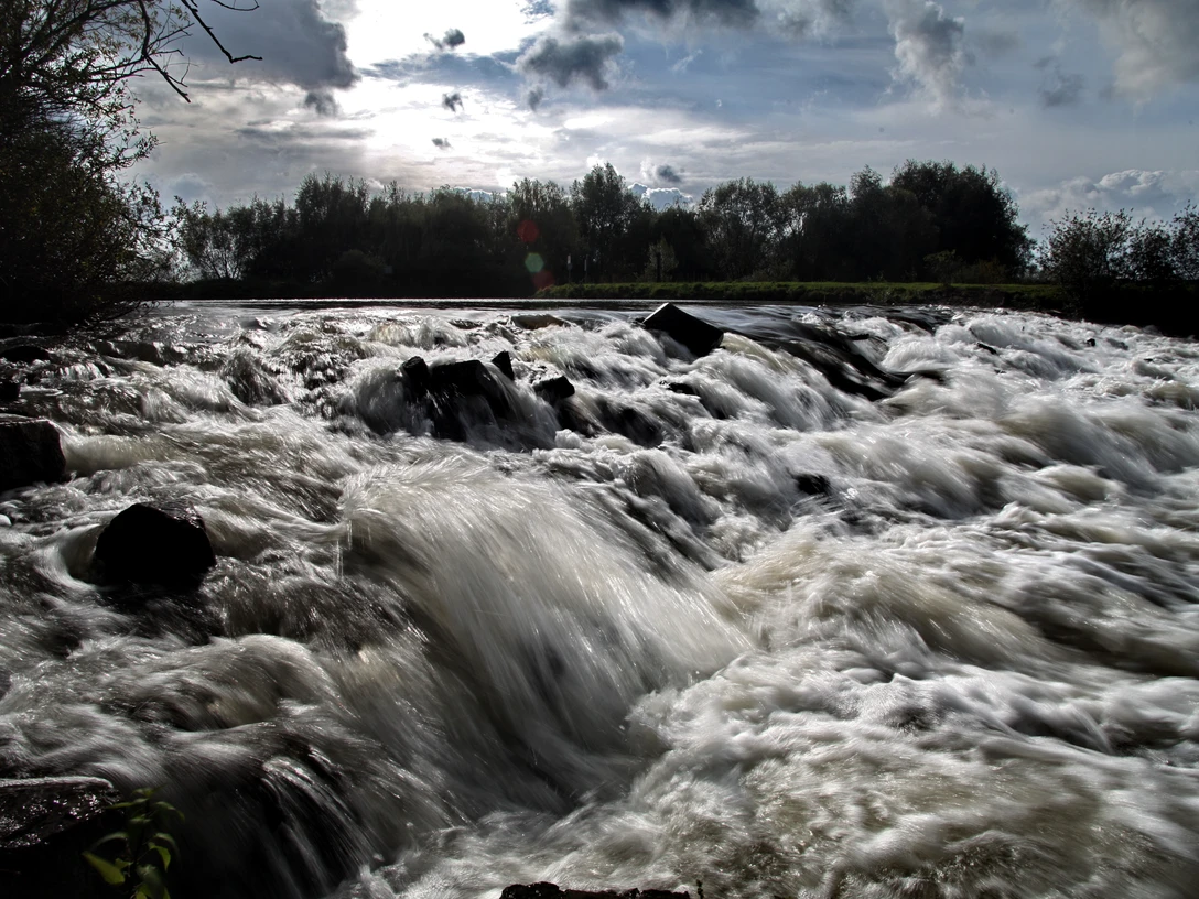 Wasserfall Neustadt a. Rbge. Tosendes Wasser fließt über dunkle Felsen in einer naturnahen Szenerie bei bewölktem Himmel.
