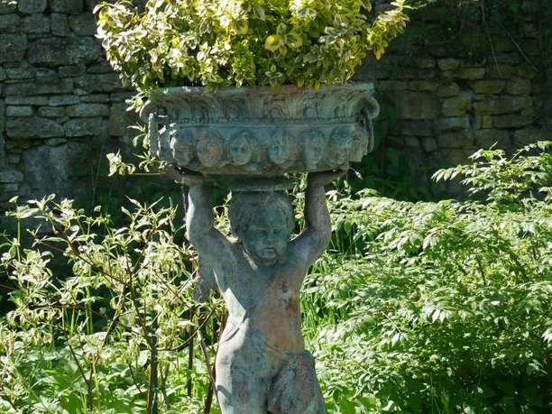 Eine steinerne Figur eines Putto trägt einen mit Pflanzen gefüllten Blumenkorb im üppigen Garten.