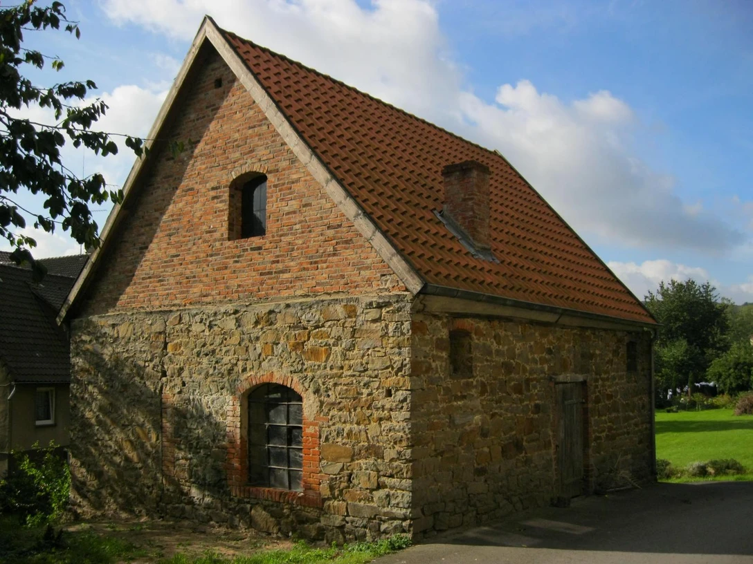 Die Alte Färbe in Extertal-Almena Steinaltes Gebäude mit Ziegeldach und kleinen Fenstern, von Sonne beleuchtet, im Grünen gelegen.