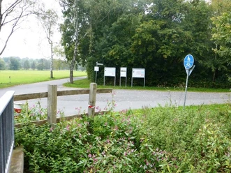 Parkplatz nahe einem Radweg am Boker Kanal, umgeben von grüner Vegetation und Hinweisschildern.