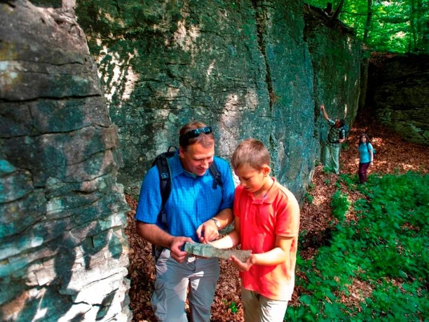 Ehemaliger Steinbruch am Hanstein bei Paderborn-Neuenbeken Ein Steinbruch mit steilen Felswänden im Wald, wo zwei Personen Steine inspizieren.