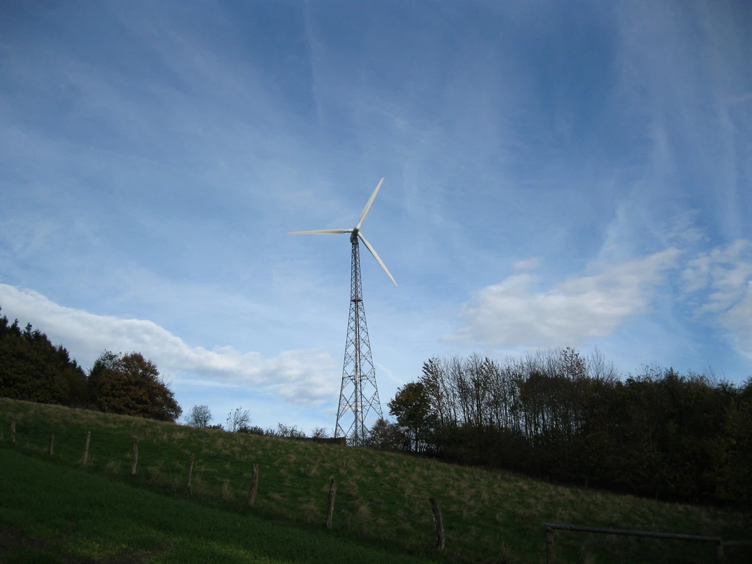 Das Windrad „SilWia“ in Extertal Ein modernes Windrad vor blauem Himmel, flankiert von Bäumen und grünem Gras in einer ländlichen Umgebung.