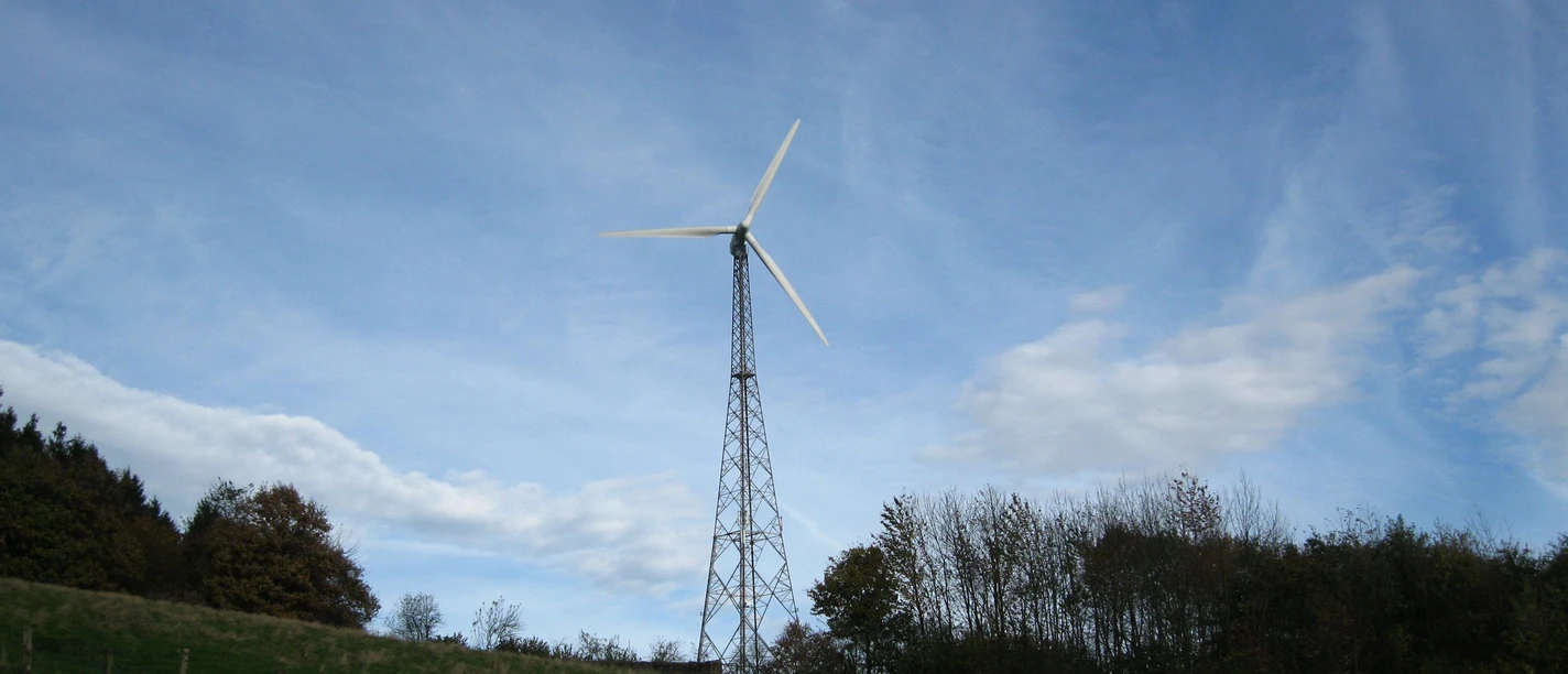 Das Windrad „SilWia“ in Extertal Ein modernes Windrad vor blauem Himmel, flankiert von Bäumen und grünem Gras in einer ländlichen Umgebung.