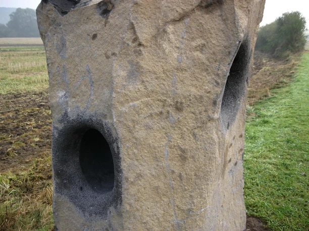 Summstein in Extertal-Laßbruch Steinerne Skulptur mit mehreren kreisrunden Resonanzöffnungen, umgeben von grüner Wiese und Ackerland.