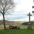 Turmberg bei Paderborn-Dahl Gedenkkreuz und Picknickbank neben einem kahlen Baum, mit Blick auf weite, hügelige Landschaft.