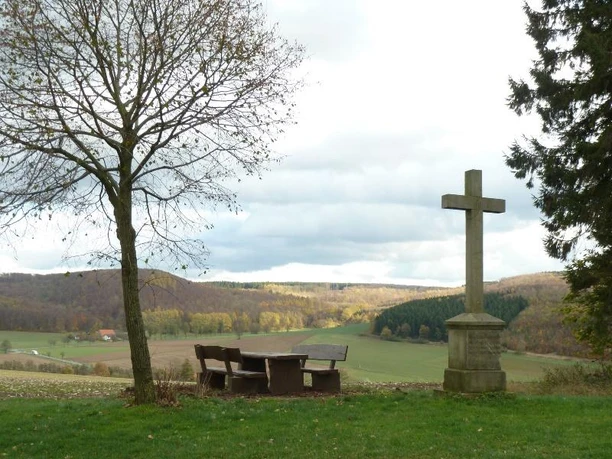 Turmberg bei Paderborn-Dahl Gedenkkreuz und Picknickbank neben einem kahlen Baum, mit Blick auf weite, hügelige Landschaft.