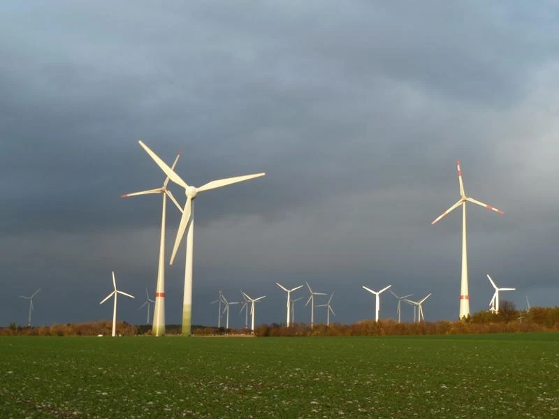 Windkraftanlagen auf grüner Wiese unter bewölktem Himmel mit mehreren Windrädern im Hintergrund.