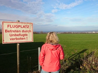 Flugplatz Paderborn-Haxterberg (Flugfeld) Eine Person blickt auf ein grünes Flugfeld mit blauen Himmel; ein Warnschild im Vordergrund.