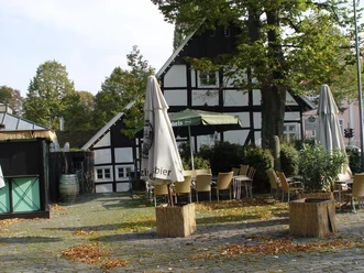 Fachwerkhaus mit Außengastronomie, Sonnenschirmen und Herbstlaub bedeckt den gepflasterten Platz.