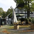 Fachwerkhaus mit Außengastronomie, Sonnenschirmen und Herbstlaub bedeckt den gepflasterten Platz.