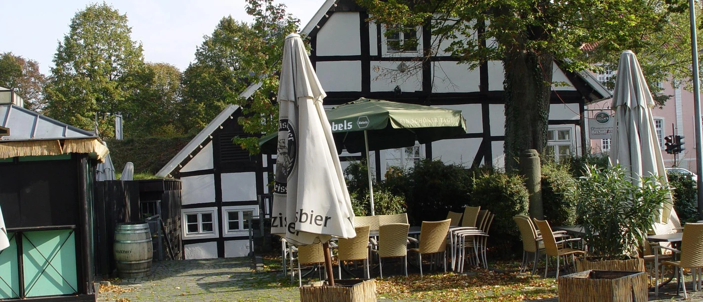 "Alte Münze" Rheda Fachwerkhaus mit Außengastronomie, Sonnenschirmen und Herbstlaub bedeckt den gepflasterten Platz.