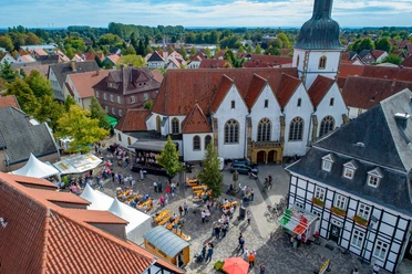 Luftaufnahme eines belebten Marktplatzes in einer historischen Stadt mit Kirchgebäude im Zentrum.
