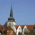 Kirche mit grünlicher Turmspitze und roten Ziegeldächern vor klarem, blauem Himmel in ländlicher Umgebung.