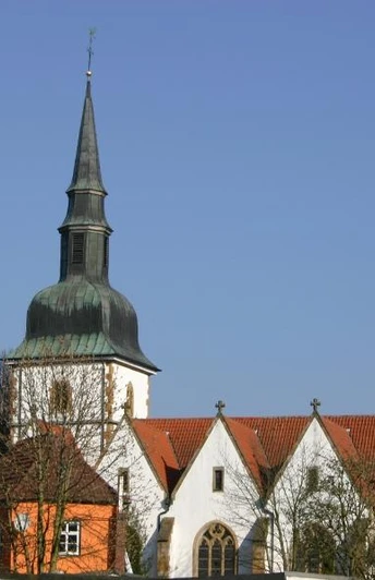 Katholische Pfarrkirche St. Johannes Baptist Kirche mit grünlicher Turmspitze und roten Ziegeldächern vor klarem, blauem Himmel in ländlicher Umgebung.