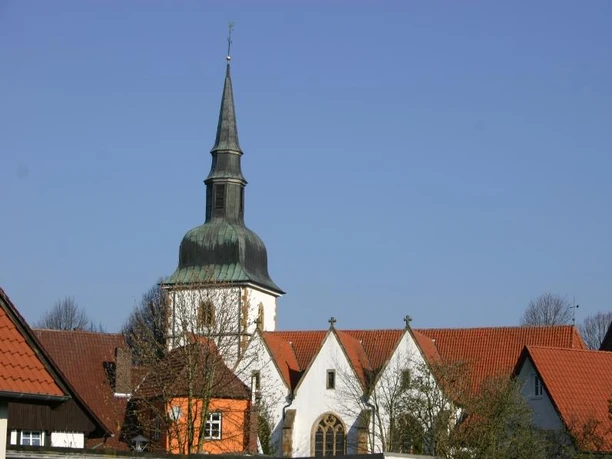 Katholische Pfarrkirche St. Johannes Baptist Kirche mit grünlicher Turmspitze und roten Ziegeldächern vor klarem, blauem Himmel in ländlicher Umgebung.