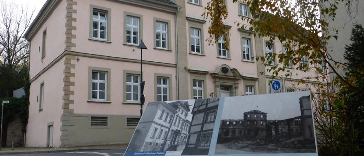Erzbischöfliches Palais (Dalheimer Hof), Außenansicht Das historische Erzbischöfliche Palais mit heller Fassade und Infotafel im Vordergrund.