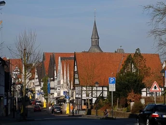 Fachwerkhäuser mit roten Dächern, ein Kirchturm, geparkte Autos und Straßenlaternen.