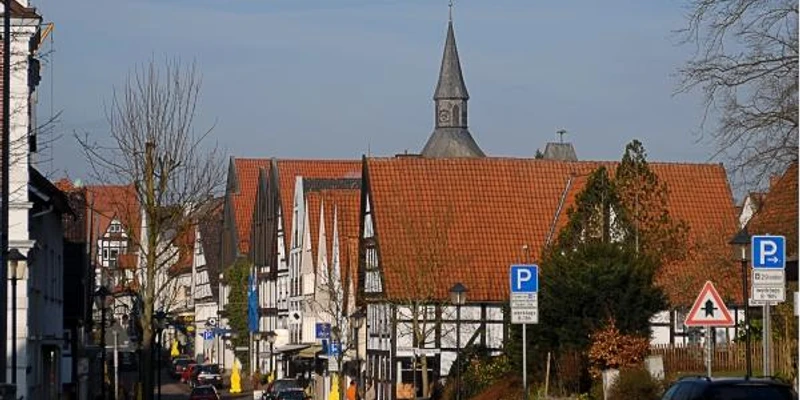 Heutorstraße / Kurzer Steinweg Fachwerkhäuser mit roten Dächern, ein Kirchturm, geparkte Autos und Straßenlaternen.