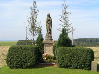 Madonnenstandbild auf einem Feld bei Paderborn-Dahl, umgeben von Bäumen und gepflegten Büschen.