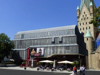 Moderne Fassade des Diözesanmuseums Paderborn neben historischer Kirche im Sonnenschein.