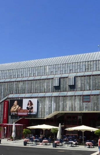 Moderne Fassade des Diözesanmuseums Paderborn neben historischer Kirche im Sonnenschein.