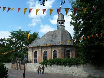 Backsteinkapelle mit oktogonalem Dachreiter, umgeben von Bäumen, mit bunten Wimpeln dekoriert.