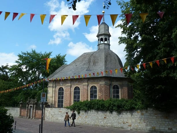 Alexiuskapelle Backsteinkapelle mit oktogonalem Dachreiter, umgeben von Bäumen, mit bunten Wimpeln dekoriert.