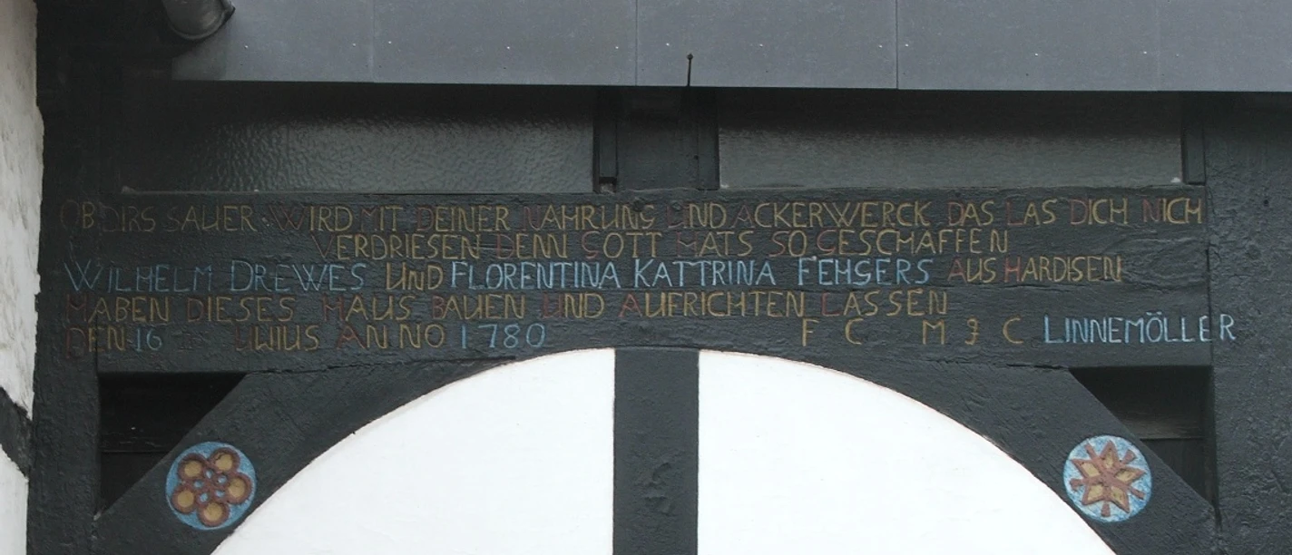 Inschrift über der Tür eines Fachwerkhauses, datiert auf 1789, mit blumenverzierten Holzdetails.