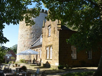 Burg Ravensberg mit massiven Steinturm und restaurierter Fassade, umgeben von grünen Bäumen.