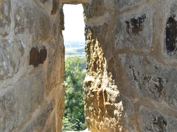 Burg Ravensberg - Blick aus dem Turm Blick durch eine kleine Öffnung einer steinernen Burgruine mit Ausblick auf grüne Landschaften.