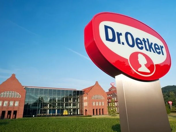 Dr. Oetker-Firmenschild vor einem modernen Gebäude mit historischen Backstein-Elementen und blauen Himmel.
