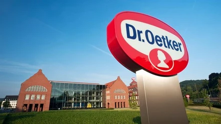 Dr. Oetker Dr. Oetker-Firmenschild vor einem modernen Gebäude mit historischen Backstein-Elementen und blauen Himmel.