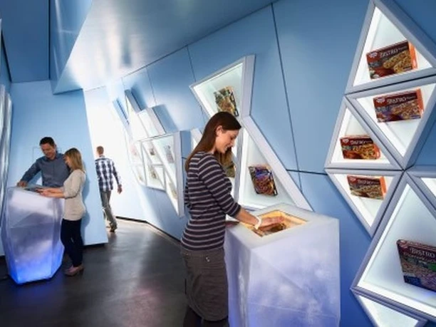 Betriebsführung in moderner Ausstellung mit beleuchteten Plakaten von Dr. Oetker Backprodukten.