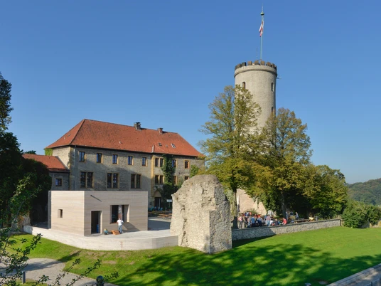 Sicht auf die mittelalterliche Sparrenburg in Bielefeld, umgeben von Bäumen bei klarem Himmel.